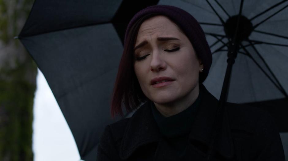Alex closes her eyes as she stands over Kara's grave in the rain.