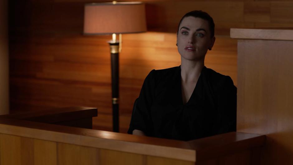 Lena sits at the stand listening to the defense attorney's question about Supergirl's identity.