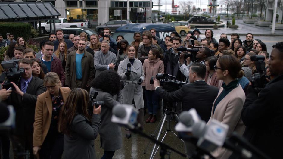 Kara pushes through the crowd as reporters wait for Supergirl's big announcement.