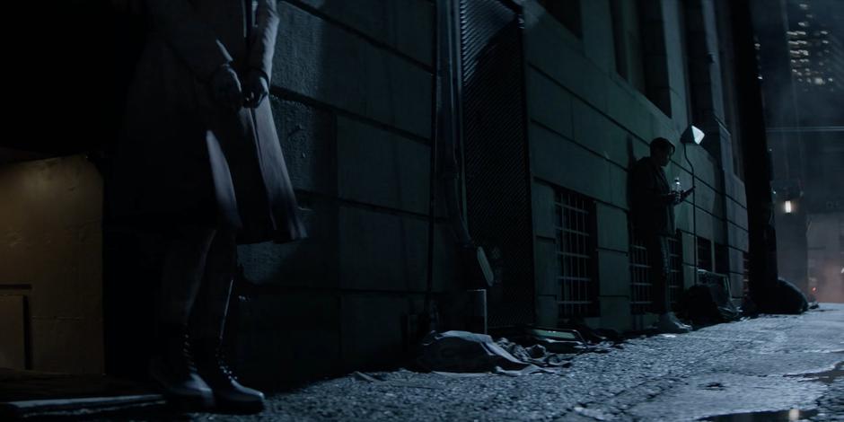 Alice steps out into the alley with her hands still bound and walks to where Kate is drinking against the wall.
