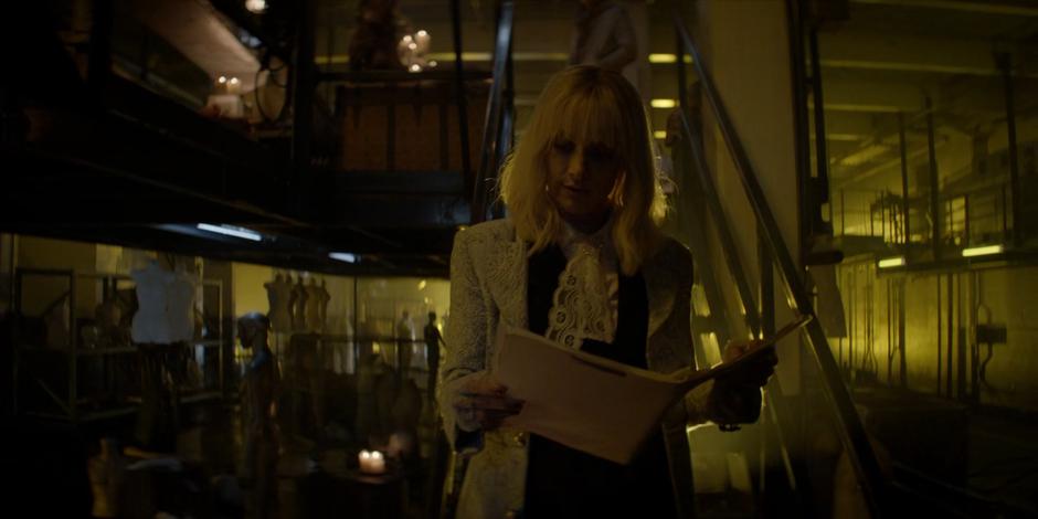 Alice reads the dossier on Dr. Ethan Campbell as she walks down the stairs.