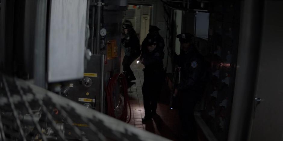 A group of police officers search the darkened warehouse for Duela Dent.