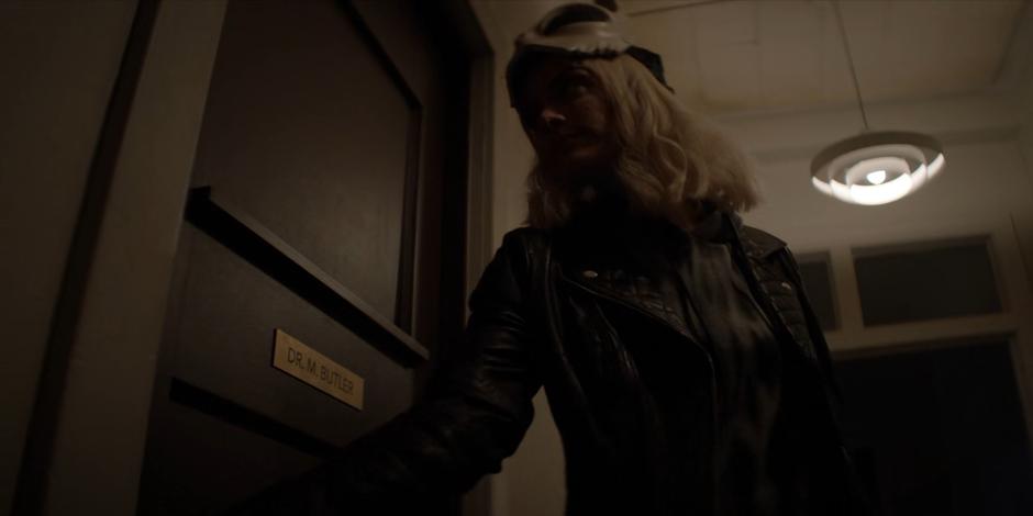 Alice opens the door to Dr. Butler's office with her mask raised.