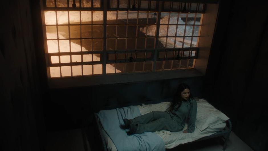 Mel sits up on a bed in a room in the psychiatric hospital.