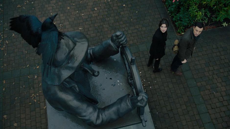 Abigael and Harry turn to look at the frozen crow atop the statue in the plaza.