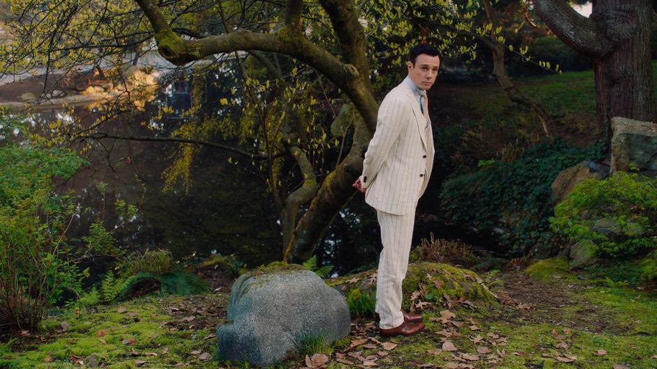 Harry turns towards the sisters from where he is standing by the pond.