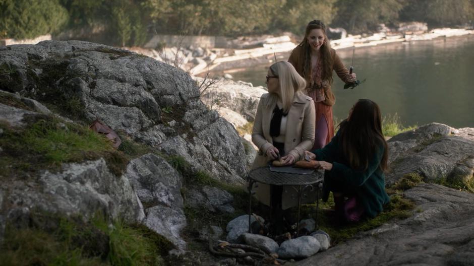 Fen shows off the knives she got from the Knife Tree to Alice and Margo who are trying to slice some bread with rocks.