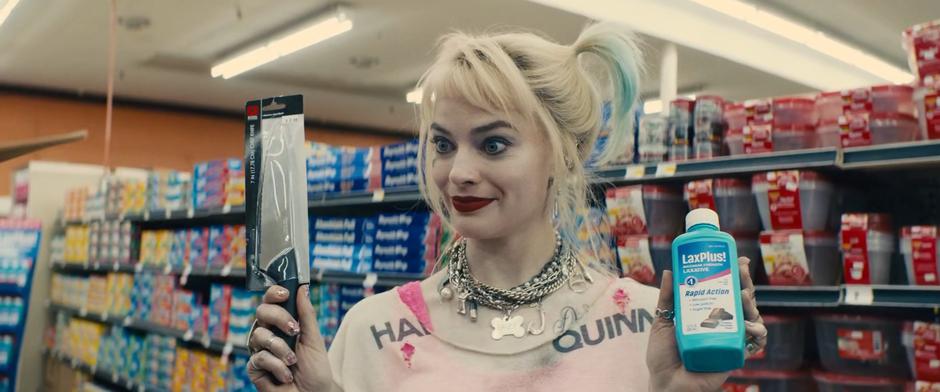 Harley holds up a knife and a bottle of laxatives and offers them as the two options for Cassandra.