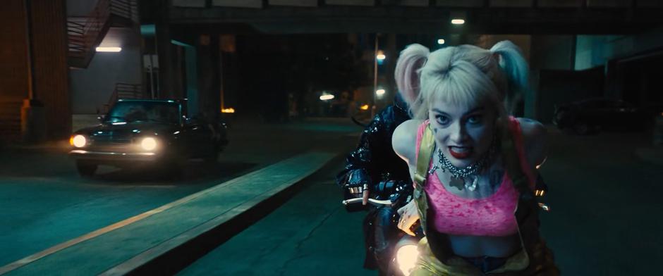 Harley is pushed on her skates in front of Helena's motorcycle while the other car drives uncontrolled behind them.