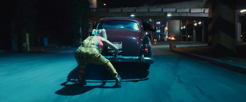 Harley skates low while holding onto the bumper of Roman Sionis's car.