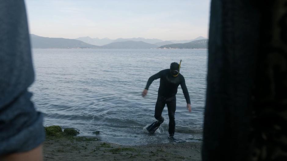 A diver walks out of the ocean in front of Eliot and Charlton.