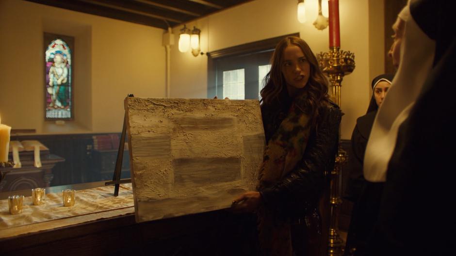 Wynonna holds up the ugly white painting to the nun welcoming her.