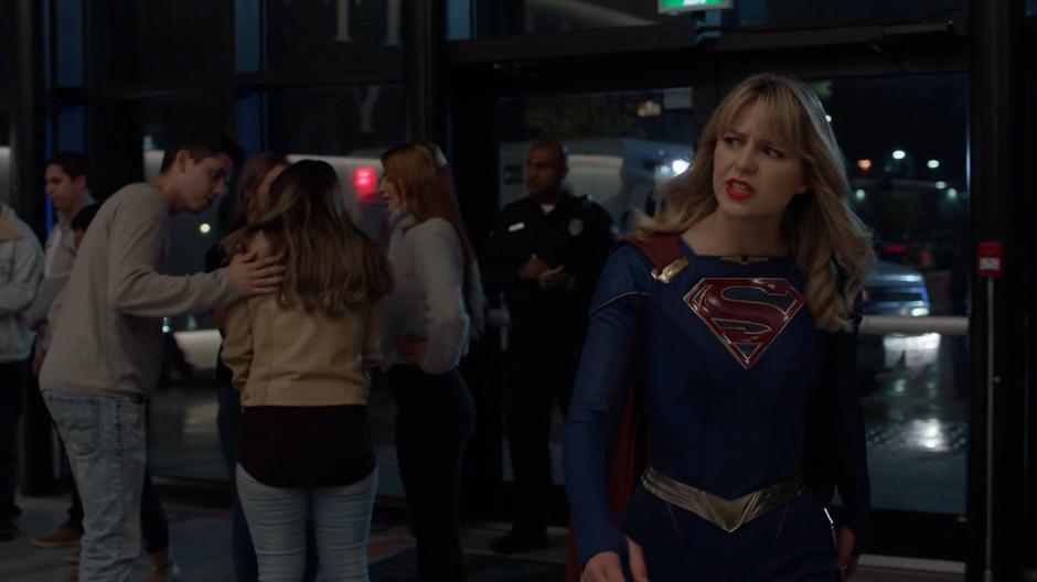 Kara walks over to Brainy in the lobby as the police question the audience members.