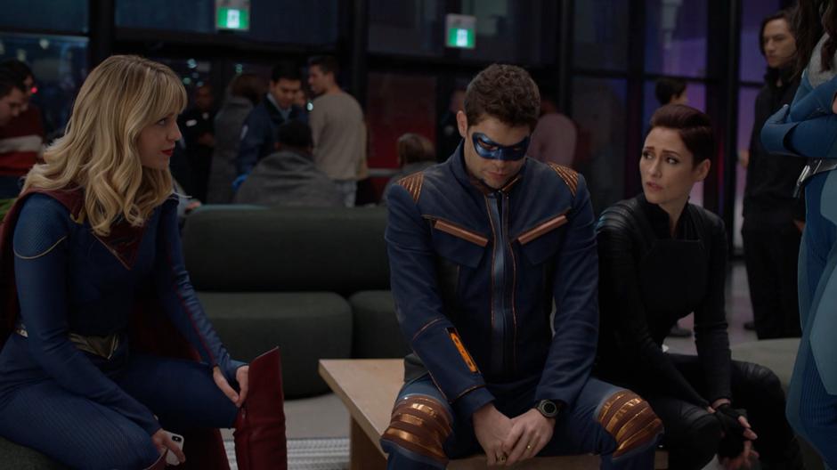 Kara and Alex sit next to Winn to comfort him.