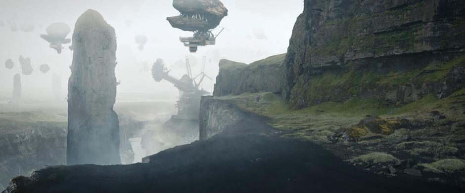 Giant mining machines sit in the distance and rocks float in the sky above the mining site.