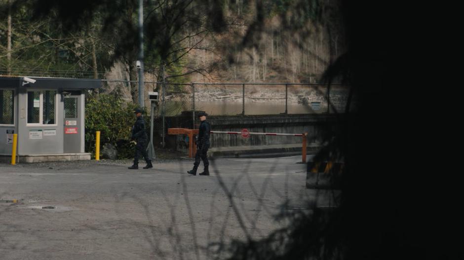 Two guards are visible at the checkpoint through the trees.