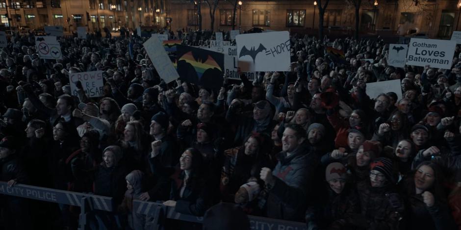 People hold up signs in support of Batwoman and chant for her return.