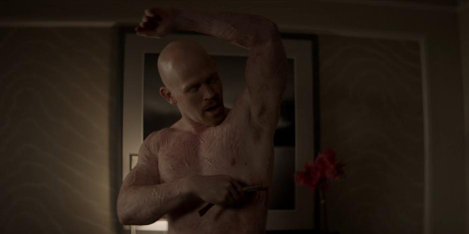 Victor Zsasz slices a new hash mark in his skin.