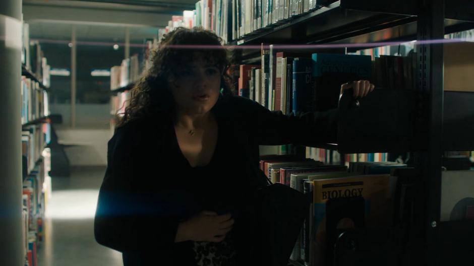 Maggie leans against a bookshelf in the library as she tries to recover from her panic attack.