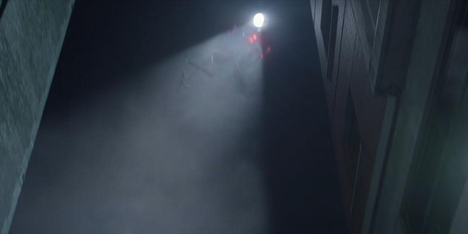 A helicopter shines its spotlight down into the alley.