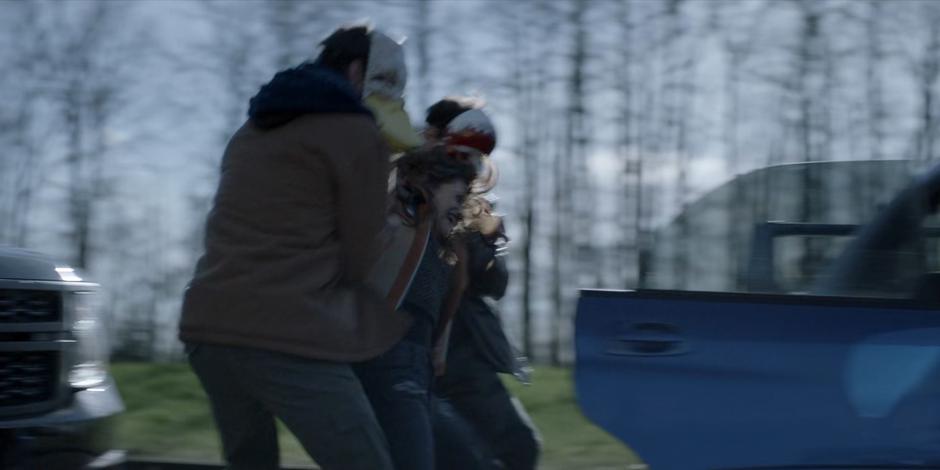 Two members of the False Face Society force Angelique into their car.