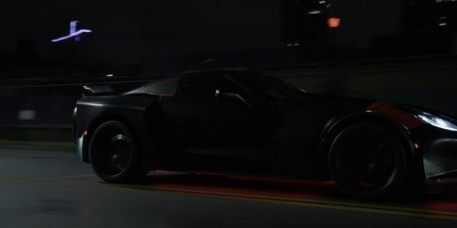 The Batmobile races down the road at night.