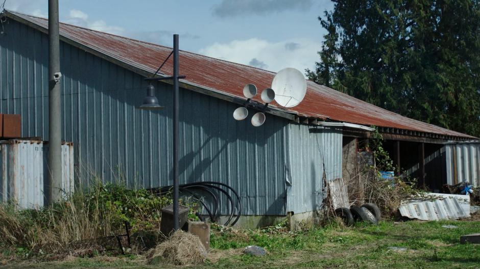 One of the farm buildings contains a security camera, large power cables, and several satellite dishes.