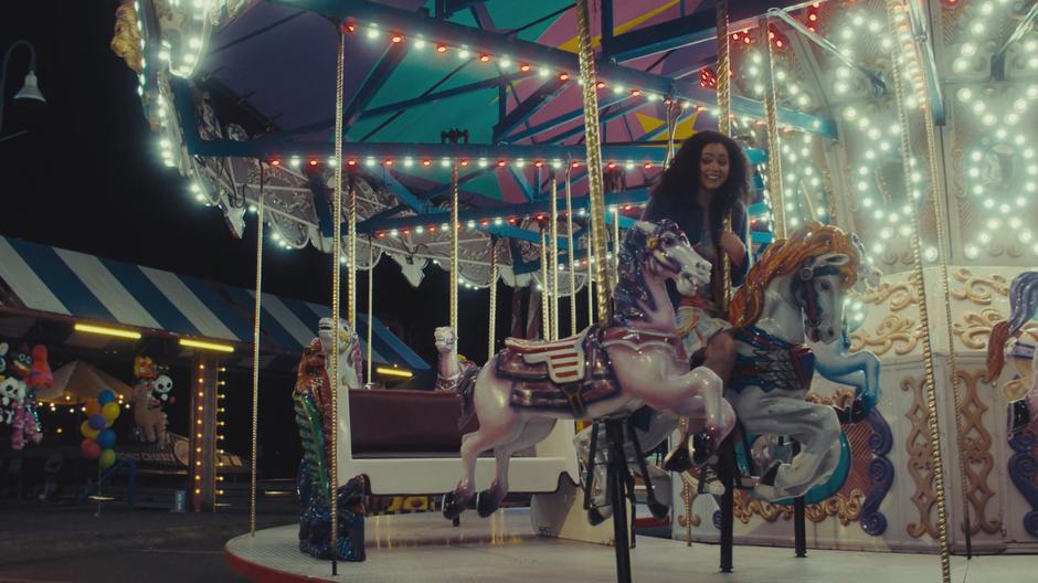 Macy sits on a horse on the carousel and calls over her sisters.