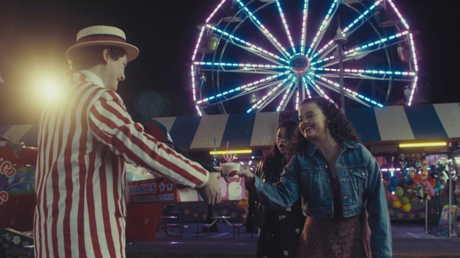 Mel watches as Maggie grabs a milkshake from the food vendor.