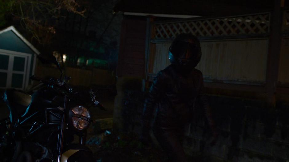 Kelly looks up at Joey's room as she walks to the back of the house still wearing her motorcycle helmet.