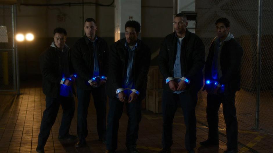 Orlando and the other four prisoners stand in the power dampening cuffs after Kara takes out their captors.