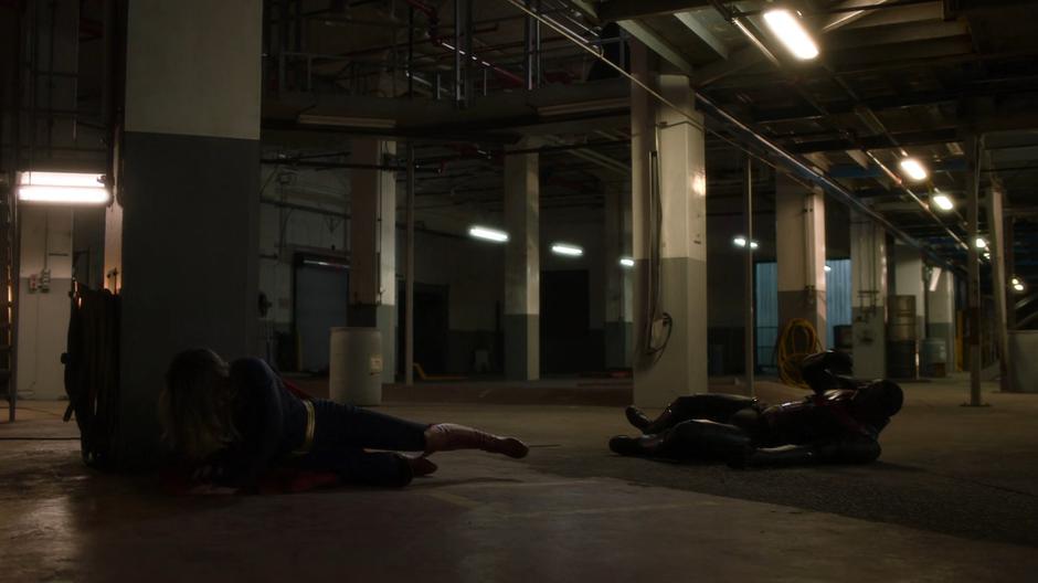 Kara and J'onn sit up after being thrown back by the fleeing prisoners.