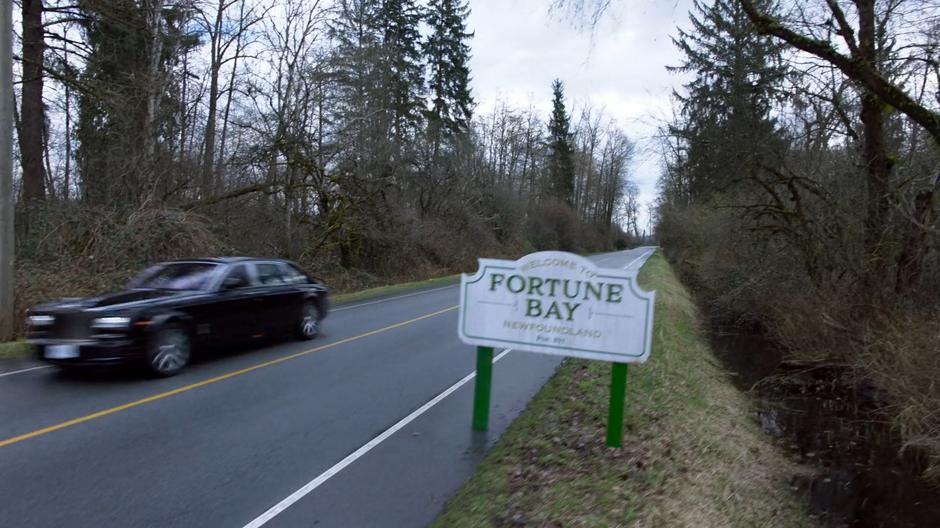 Lena's car drives past the Welcome to Fortune Bay sign on her way out of town.
