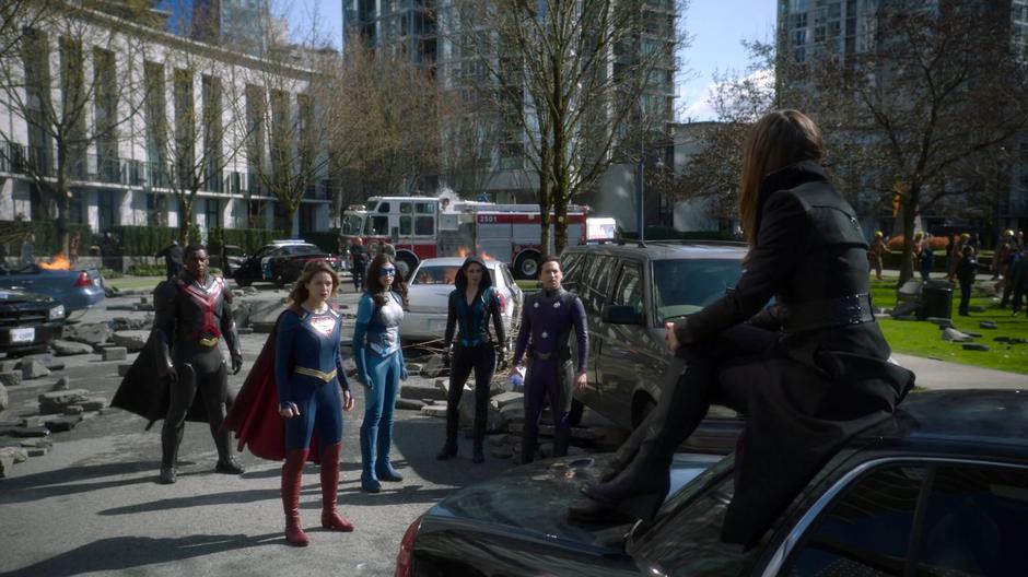 J'onn, Kara, Nia, Alex, and Brainy turn to find Nxyly watching them from atop a car after they defeated her cat.
