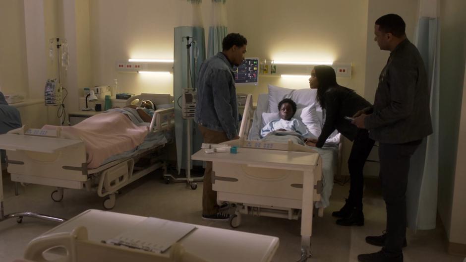Kelly leans over Joey's bed while talking with Orlando and Diggle.