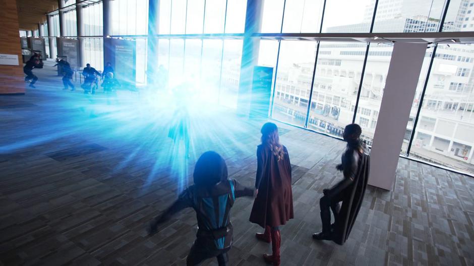 Alex, Kara, and J'onn lean back as the totem that Nxyly is holding bursts into a bright blue light.