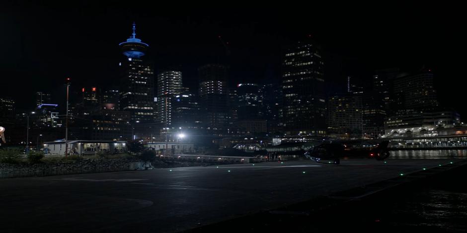 A helicoper lands on a waterfront helipad at night.
