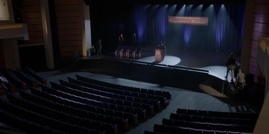 Liam Crandle stands on stage as several guards approach from all sides.