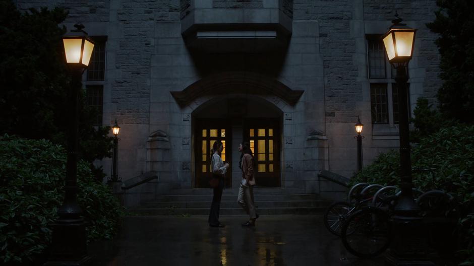 Nia and Maeve walk outside the hall at night.