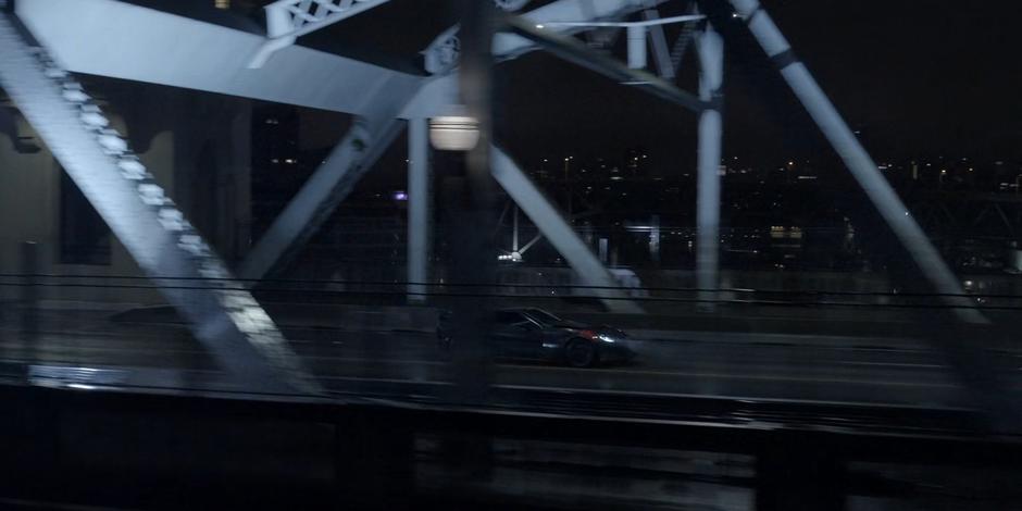 The Batmobile speeds down the center of the bridge.