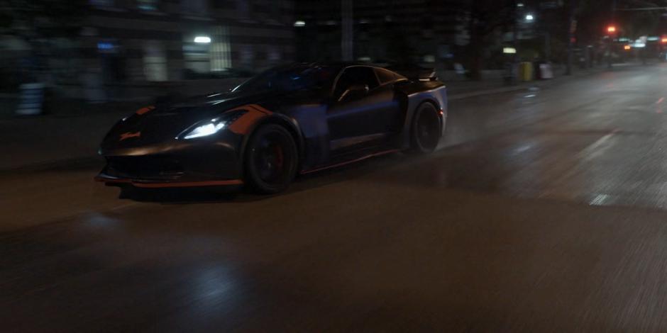 The Batmobile races down the street at night.