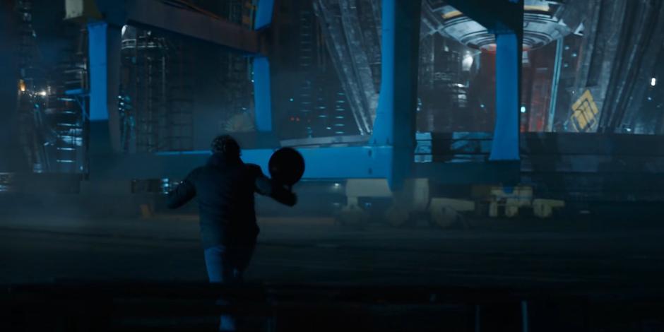 Dan runs across the docks towards a blue crane while holding his wok.