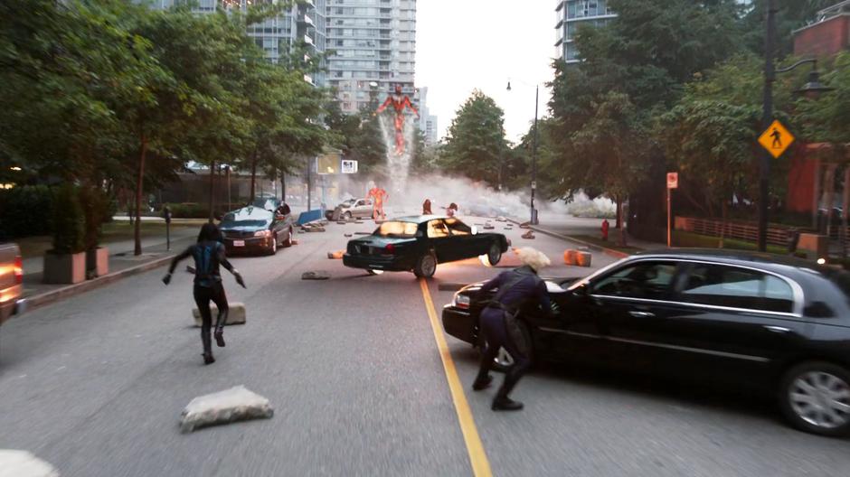 Alex runs forward and Brainy takes cover as a flying robot blows up a car during the battle in the street.