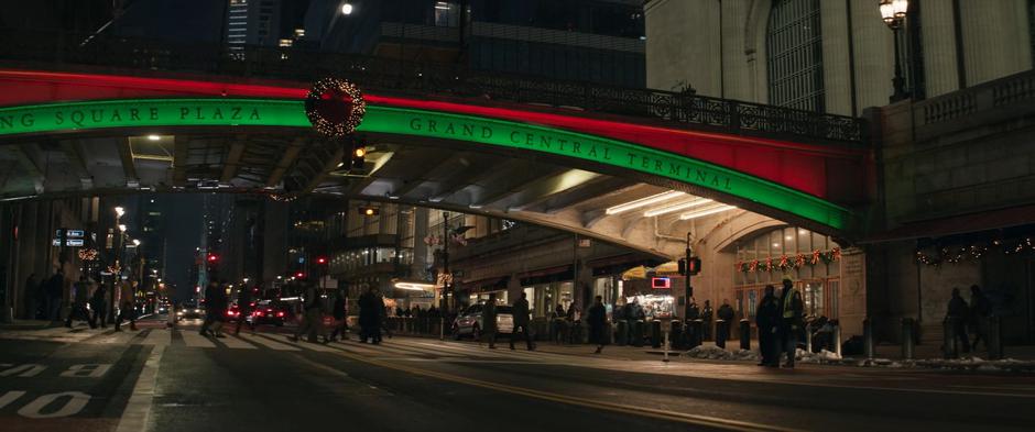 Kate leaves the terminal and crosses the street beneath the Pershing Square bridge which is lit in red and green.