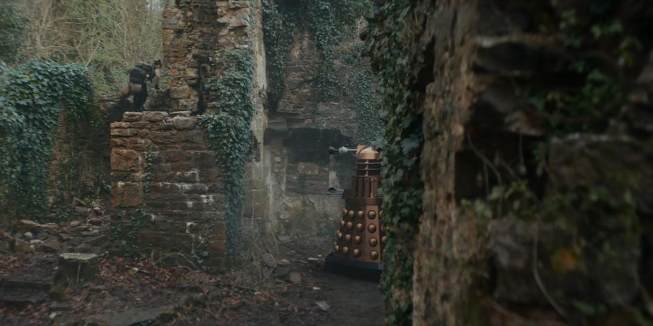 Bel climbs out of the ruins through the back wall as a Dalek floats in.