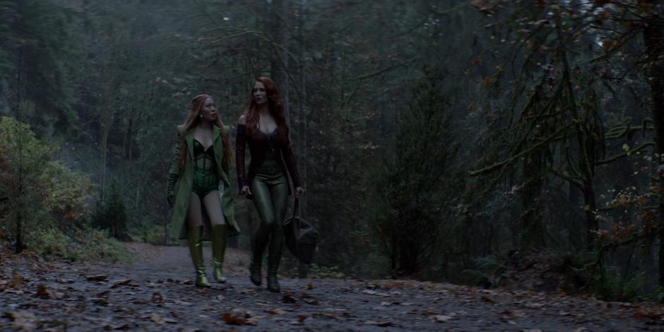 Mary listens to Pam while they walk down a road in the woods.