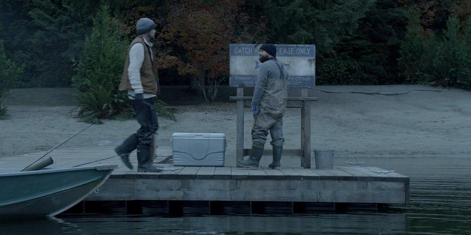 Two fishermen prepare their catch in front of a sign delaring the lake "Cath and Release Only".