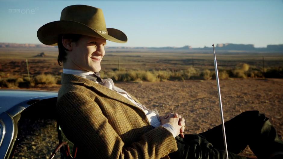 The Doctor waits for his friends on the hood of his car.