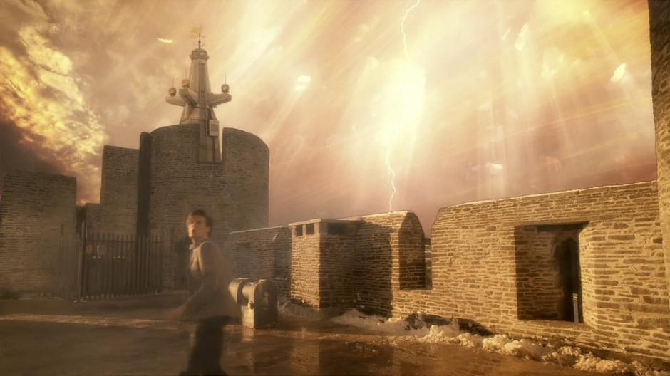 The Doctor runs to the weather machine tower while a storm brews overhead.