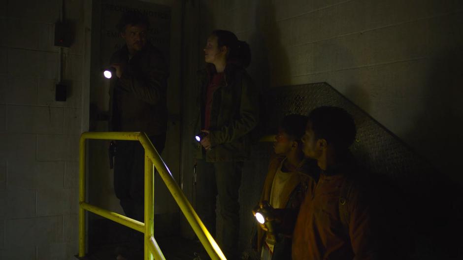 Joel looks at Ellie after seeing she was keeping her gun in her jacket pocket while Sam and Henry wait to head down into the tunnel.